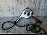 Side view of vintage metal and wooden hairdryer with long cloth-covered cord.