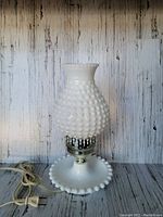 Front view of vintage milk glass hobnail lamp showing white textured glass and base with electric cord and plug.