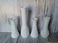 Front view of four vintage milk glass vases in various shapes and sizes against a rustic wooden backdrop.