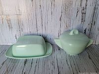 Side by side view of the mint green Melmac butter dish and sugar bowl with lids against a rustic wooden background.