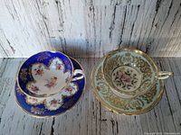 Top view of two vintage Paragon teacup and saucer sets showing detailed floral and gold designs with one commemorative for Queen Elizabeth II.