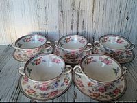 Five vintage Royal Doulton shallow double handled cups with matching saucers, arranged in a group, showing floral pattern and gold trim on white china.