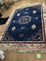 Full view of navy blue and tan Asian motif area rug with fringe on wooden floor