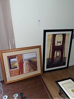 Two framed art prints leaning against a wall, one beachside print and one Golden Gate Bridge print.
