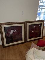 Two framed floral prints with dark red backgrounds featuring floral arrangements, each in textured wide wood-like frames.