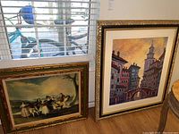 View of both framed artworks, the larger colorful Norwegian sun print and smaller Goya canvas print on floor near window.