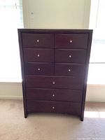 Front view of brown stained wood chest with 8 drawers and chrome hardware, showing slight surface scratches.