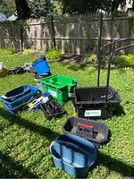 Wide view of cleaning supplies arranged on grass including blue, green, and black buckets and bins, cleaning brushes, and a rolling bucket cart with handle.