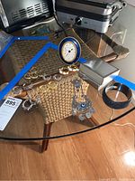 Glass table displaying assorted costume jewelry, a small clock, and napkin rings