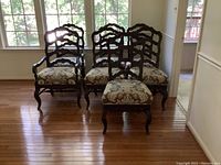 View of five dining chairs and two captain chairs arranged with a window backdrop showing wood floor and light through windows.