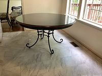 Full view of round wood top dining table with glass cover and metal curved base, showing design and overall condition.