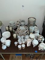 Stoneware plates, bowls, mugs, and assorted dinnerware displayed on a table, showing full collection with floral designs and varied shapes.
