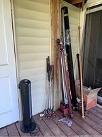 Photo showing black Lasko tower fan, golf clubs leaning against wall, wooden curtain rods in different finishes, and Santa decorative sign.