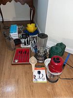 Overview of various kitchen items on floor including the blender, cast iron pan, canisters, quad chop, flatware, and kitchen utensils.