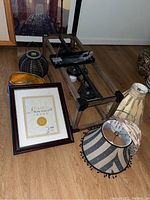 View of the box chandelier light fixture frame with three light sockets and hanging chains, multiple fabric lamp shades, a framed certificate, and ceramic decorative vases on wooden floor.
