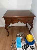 Full view of the Biggs wooden side table with three drawers, showing top, legs, and drawers. Various kitchen items placed around the base of the table.