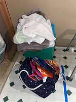 Stack of towels in various colors on a green plastic storage bin and reusable shopping bags on the floor in front of it.