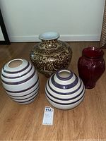 Overview of four vases on floor including brown and white patterned vase, two white with purple striped vases, and one dark red glass vase