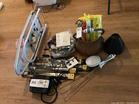 Lot laid on floor showing copper coal bucket with faux logs, two Goodyear windshield wipers (9 and 22 inch), mini ironing board, white measuring spoons, black cone-shaped emergency light, vacuum parts including charger, metal rug beaters, and other small items.