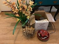 Glass bowl centerpiece with faux flowers set on wood slices, jar of natural items beside a cardboard box and tabletop fountain in background