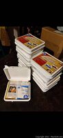 Stack of ten white plastic Auto First Aid Kits with one open showing contents including bandages and wipes.