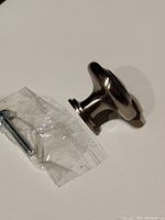 Side angled view showing round nickel pull and mounting screw in plastic packaging
