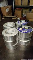 12 rolls of aluminum foil tape stacked on a dark surface with some packaging damage visible.