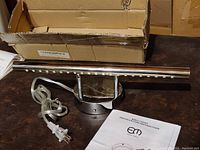 Photo of the 16 inch chrome vanity light, showing power cord, round base, and LED light bar with original packaging and instruction manual.