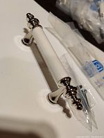 Close-up of one chrome and white Amerock cabinet/drawer pull showing chrome decorative ends and white middle section, includes accompanying screws.