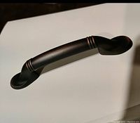 Single Amerock cabinet drawer pull showing curved design with ridged accent bands and dark rubbed bronze finish.