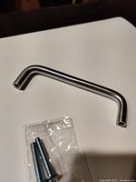 Close-up photo of a single Amerock nickel finish cabinet/drawer pull with mounting screws in original packaging.