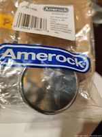 Photo of Amerock branded package showing one round chrome cabinet pull inside original plastic packaging.