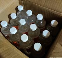 Open box showing multiple transparent plastic bottles with white caps filled with clear liquid, presumably hand sanitizer gel.