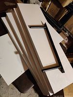 Four white floating shelves stacked, showing the length, width and edges, along with one black mounting bracket laid on top.