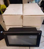 Five white boxes stacked with one black rectangular outdoor light in front; showing packaging and single unit shape and size.