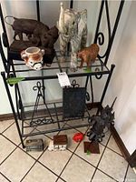Wide shot showing all figurines and items on metal rack and floor, including wooden elephant, bull figurine, bull coffee cup, metal soldier, frame holders, piggy banks
