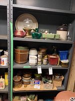 Shelving unit with assorted planters, ashtrays, glass globe, stoneware jug, and candle holders arranged on shelves.