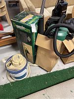 Photo of Poulan Pro Woodsman Chainsaw boxed with two shop vacuums and astroturf rolls in background.