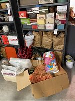 Shelving unit containing assorted shoe boxes, paper goods, metal trash can, shoe racks, fabric, and a floral tin container.