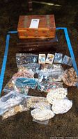 Full view of jewelry lot spread out on carpet, showing cedar lined box, individually bagged jewelry including pearl necklaces, beads, chains, rings, and pins.