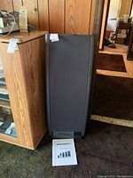 Floor-standing Dahlquist speaker with owner's manual on carpet next to wooden cabinet
