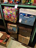 Boxes of sewing materials on shelving showing various cardboard boxes, some labeled and one floral patterned, containing sewing materials and patterns.