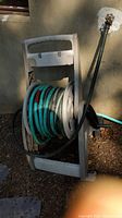 Gray plastic hose reel holding a coiled green garden hose next to an outdoor spigot.