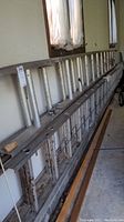 Two aluminum extension ladders leaning against a wall, showing some dirt and wear.