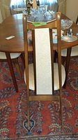 Single dining chair back with wood frame and beige fabric center panel; table edge and glassware in background.