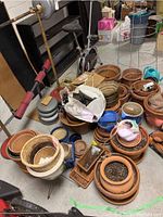 Wide view of terra cotta and glazed ceramic pots, metal tomato cage, and other accessories on floor.