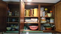 Full view of upper cabinets containing pitchers, nesting bowls, linens, glassware, and containers