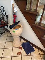 Photo of two umbrellas and a smaller one in the concrete planter, with raincoat and rain bonnets on the floor nearby.