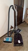 Full view of Kenmore canister vacuum with hose and wand, and desk lamp on carpeted floor