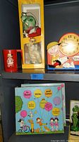 Shelved vintage items including boxed frog puppet, Peanuts alarm clock, and red Peanuts mug.